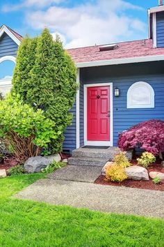 a blue house with red door and landscaping in the front yard, on a sunny day