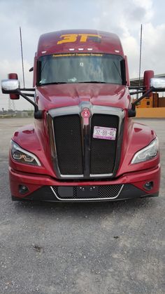 the front end of a red semi truck parked in a parking lot with other trucks behind it