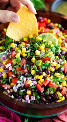 a person dipping a tortilla into a bowl filled with black beans, corn and cilantro