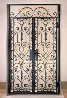 an ornate wrought iron gate with gold and white flowers on the top, in front of a beige wall