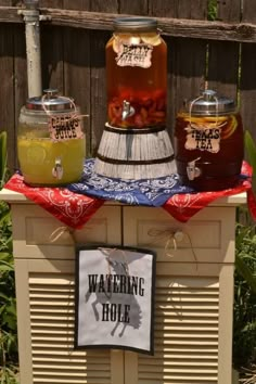 three jars filled with liquid sitting on top of a wooden table in front of a fence