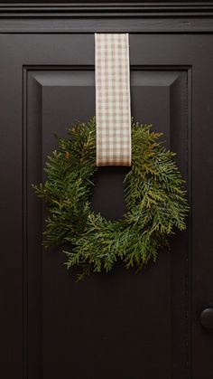 a wreath hanging on the front door with a checkered towel hung from it's side