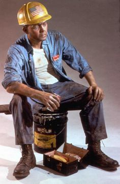 a man wearing a hard hat sitting on top of a barrel next to a bucket