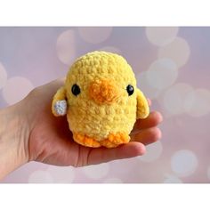 a hand holding a small yellow crocheted chick with black eyes and an orange beak