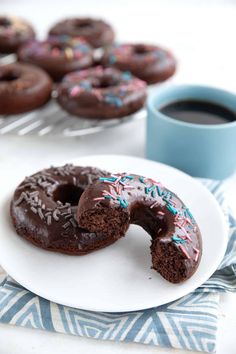 two chocolate donuts on a white plate with one bite taken out and coffee in the background