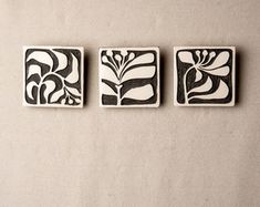 three black and white tile designs on a beige background, each with an abstract flower design