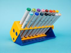 there are many pens in the holder on the blue table top and one is yellow