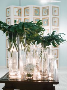 there are many vases with plants and candles on the table in front of them