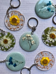 six glass keychains with flowers on them are hanging from a brick wall in front of a white brick wall