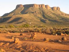 a mountain range with rocks in the foreground and bushes on the far side, surrounded by scrub brush