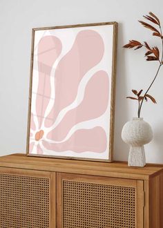 a wooden cabinet sitting next to a white vase with a plant in front of it