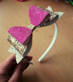 a person is holding up a pink and gold bow headband on a wooden table