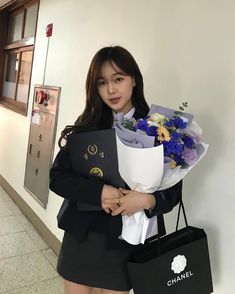 a woman holding flowers and shopping bags in an office building hallway while standing next to a wall