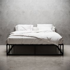 a black and white photo of a bed with two pillows on top of it, in front of a concrete wall