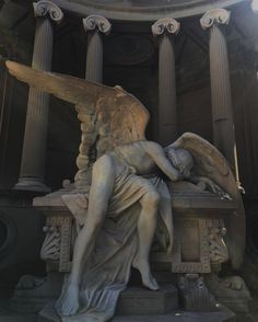 an angel statue sitting on top of a bench in front of some pillars and columns