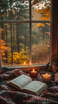 an open book sitting on top of a bed next to a window with candles in it