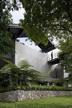 the house is surrounded by lush green trees and rocks, with a man standing on the balcony