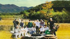 a group of people posing for a photo in front of some hills and trees with mountains behind them