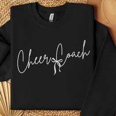 a black sweatshirt with the word cheer coach on it next to some straws and a fan