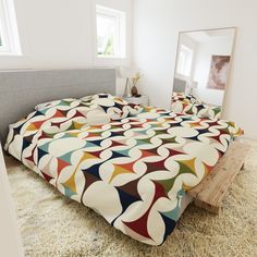 a bed with a colorful comforter on top of it next to a mirror in a room