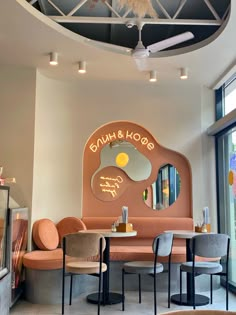 the interior of a restaurant with round tables and chairs, an egg shaped sign on the wall