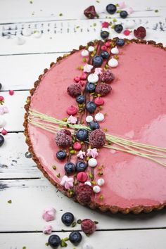 a pink cake with blueberries, raspberries and other toppings on it