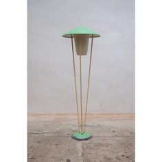 a green floor lamp with two wooden sticks sticking out of it's sides on concrete