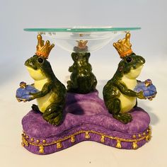 two frog figurines sitting on top of a purple table with a glass bowl