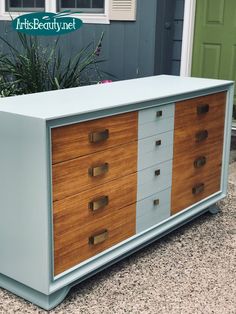 an old dresser is painted blue and has wooden drawers on it with brass handles, along with a plant in front of the door