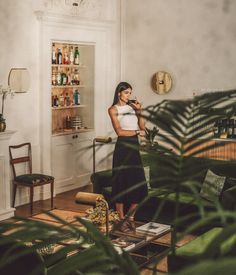 a woman standing in a living room next to a plant