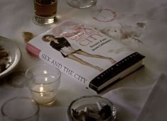 a table topped with books and candles next to glasses on top of a white cloth