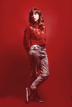 a woman standing in front of a red background with her hands on her hips and looking at the camera