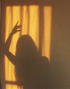 the shadow of a woman standing in front of a window holding her hand up to the side