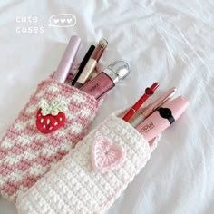 a pink and white knitted pencil holder with lipstick, eyeliners and pens in it