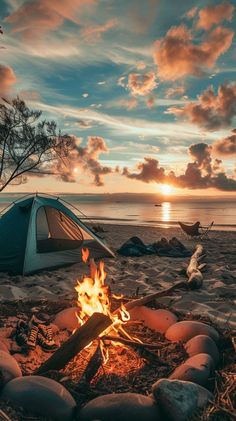 there is a campfire on the beach with a tent in the background at sunset