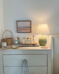 a white dresser with some bottles on it and a lamp in the corner next to it