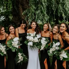 a group of women standing next to each other in front of a tree holding bouquets