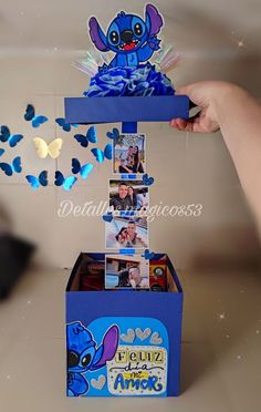 a person holding up a blue box with pictures on it and butterflies flying around the top