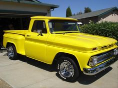 an old yellow pickup truck parked in front of a house