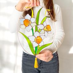 a woman is holding up a stained glass piece with daffodils on it