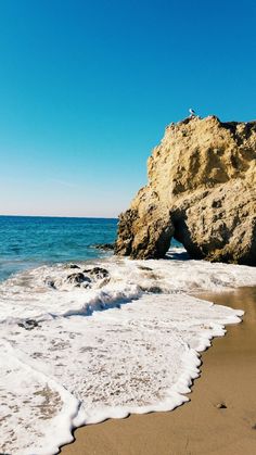 a person standing on top of a rock formation near the ocean with foamy water