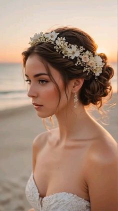 a woman wearing a wedding dress on the beach with her hair up in a bun