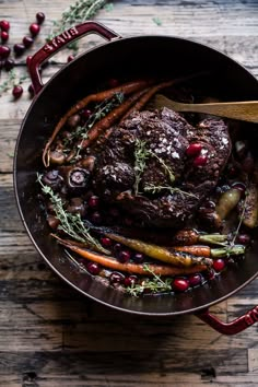 a pot filled with meat, carrots and cranberries on top of a wooden table