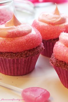 three cupcakes with pink frosting and sprinkles sitting on a plate