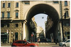 an arch in the middle of a street with cars driving under it and people walking on the sidewalk below