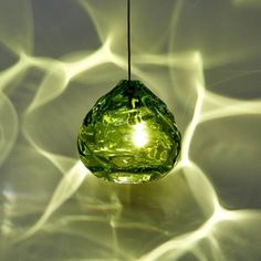 a green light bulb hanging from a string in front of some wavy lightshades