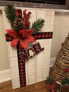 a wooden cross decorated with red and black plaid ribbon, pine cones, evergreens and a bow