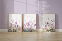 three framed art pieces on a wooden floor in front of a wall with purple flowers