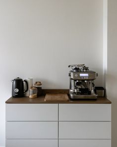 a coffee maker sitting on top of a wooden counter next to a white cabinet with drawers