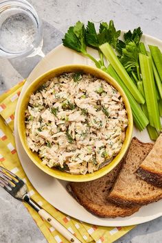 a bowl of chicken salad with bread and celery on a plate next to a glass of water